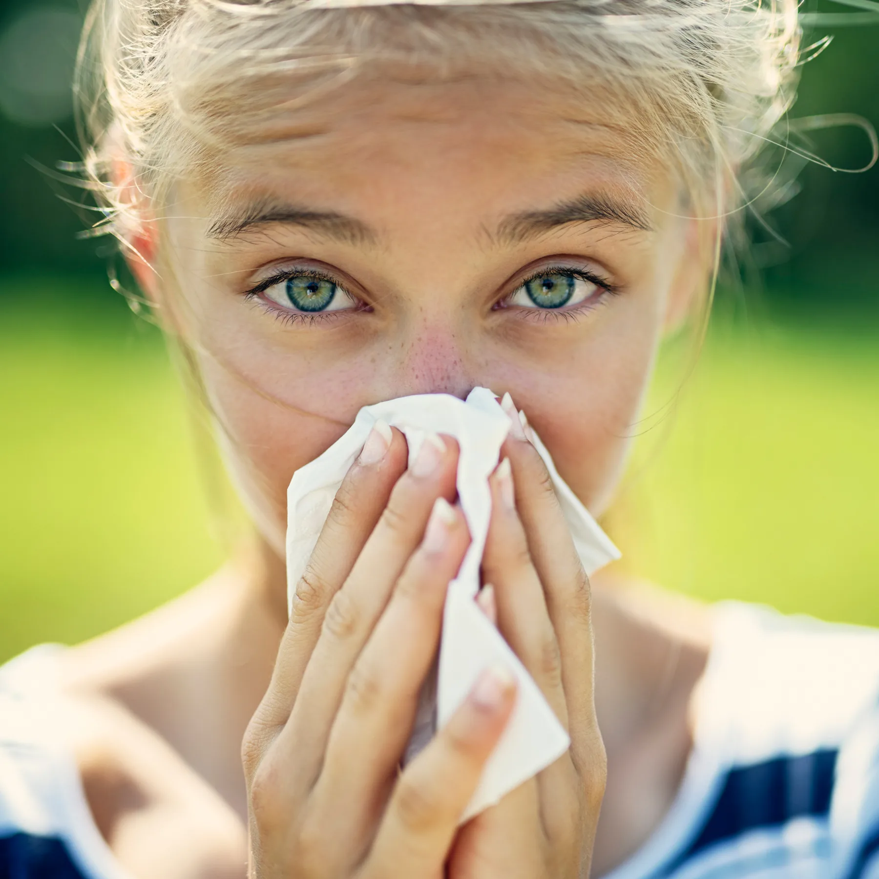 Portraitaufnahme einer jungen Frau, die in die Kamera schaut und die Nase putzt.