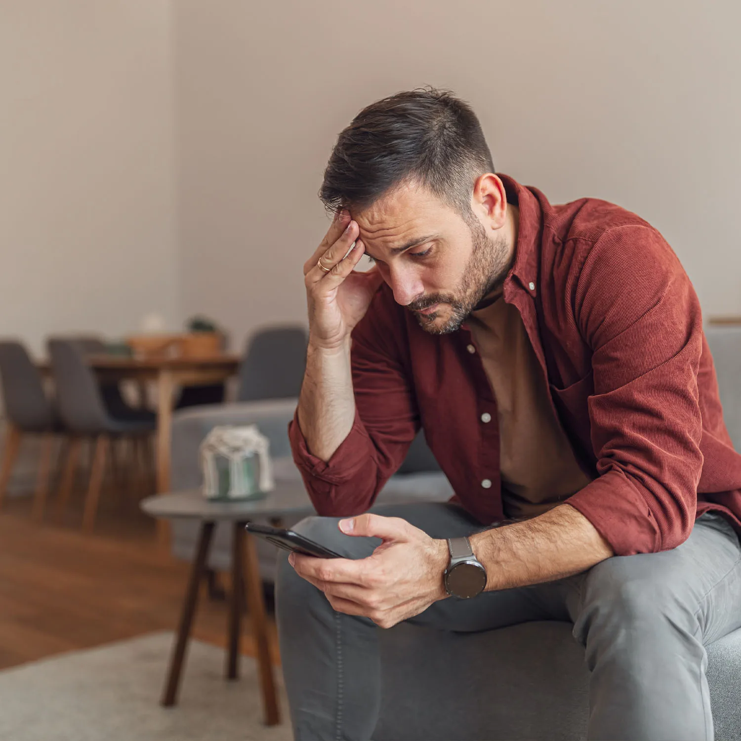 Ein Mann, der gestresst auf sein Handy schaut und sich den Kopf hält.